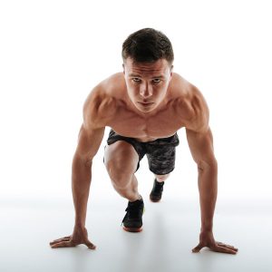 Close-up of young handsome runner with short haircut standing in start position, looking at camera, isolated on white background