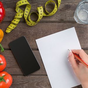 Concept diet, slimming plan with vegetables top view mock up. A female hand in a sports bracelet writes an article about proper nutrition