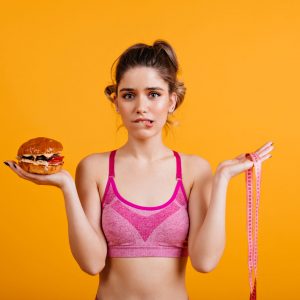 Hesitating woman holding cheeseburger. Studio shot of caucasian girl on diet.