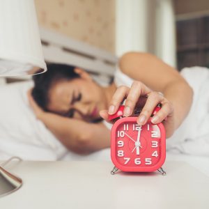 Lazy woman hand holding alarm clock on the bed